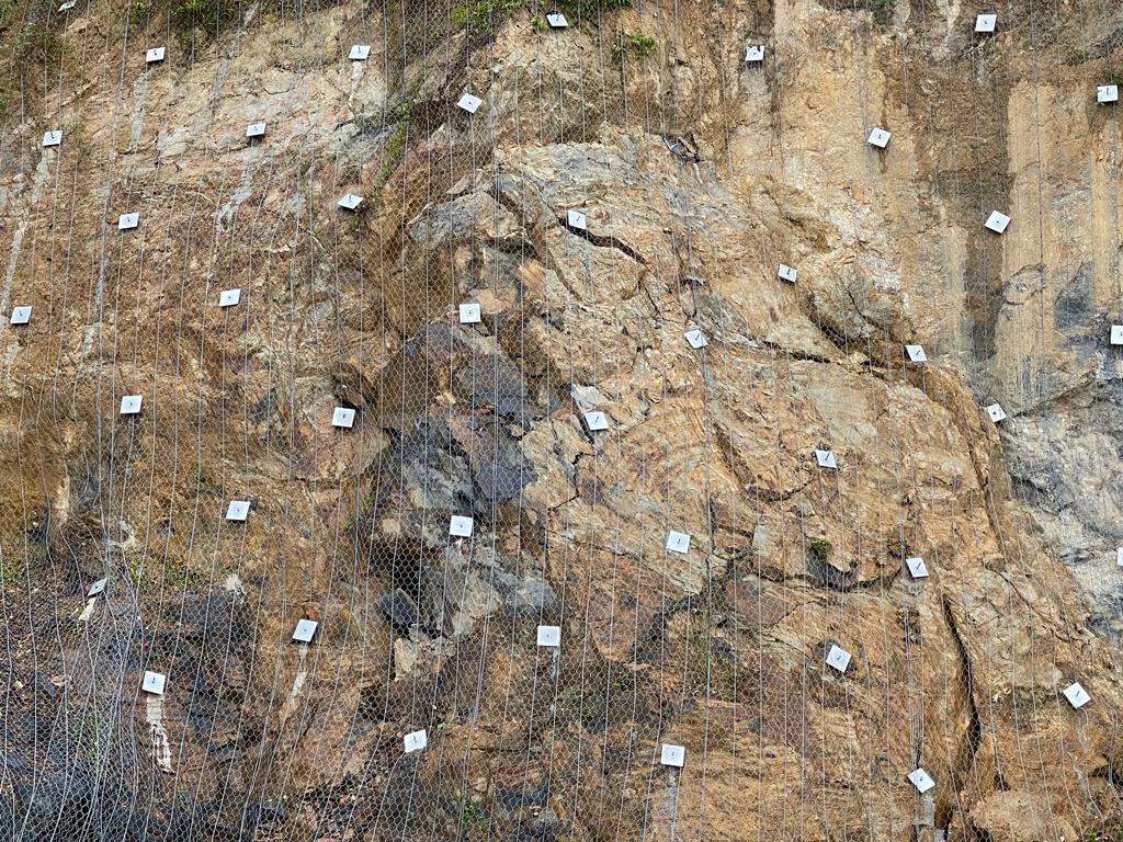 Close-up of anchored wire mesh netting stabilizing a rock slope face